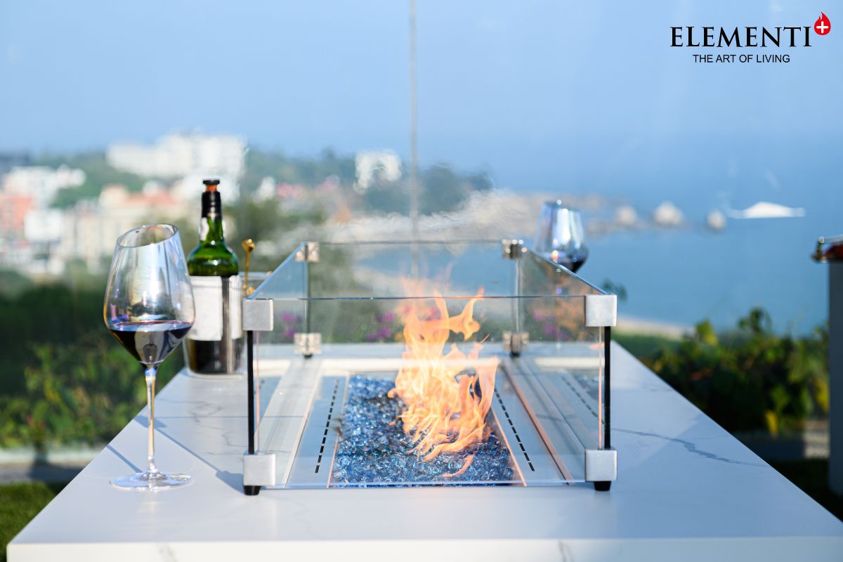 The lit fire of the CARRARA table with the glass wind guard