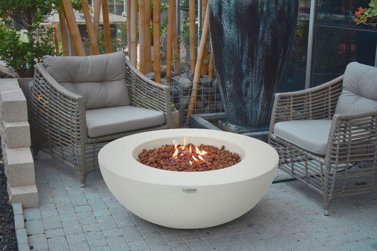 LUNAR BOWL Cream White fire pit in a garden with wicker seating