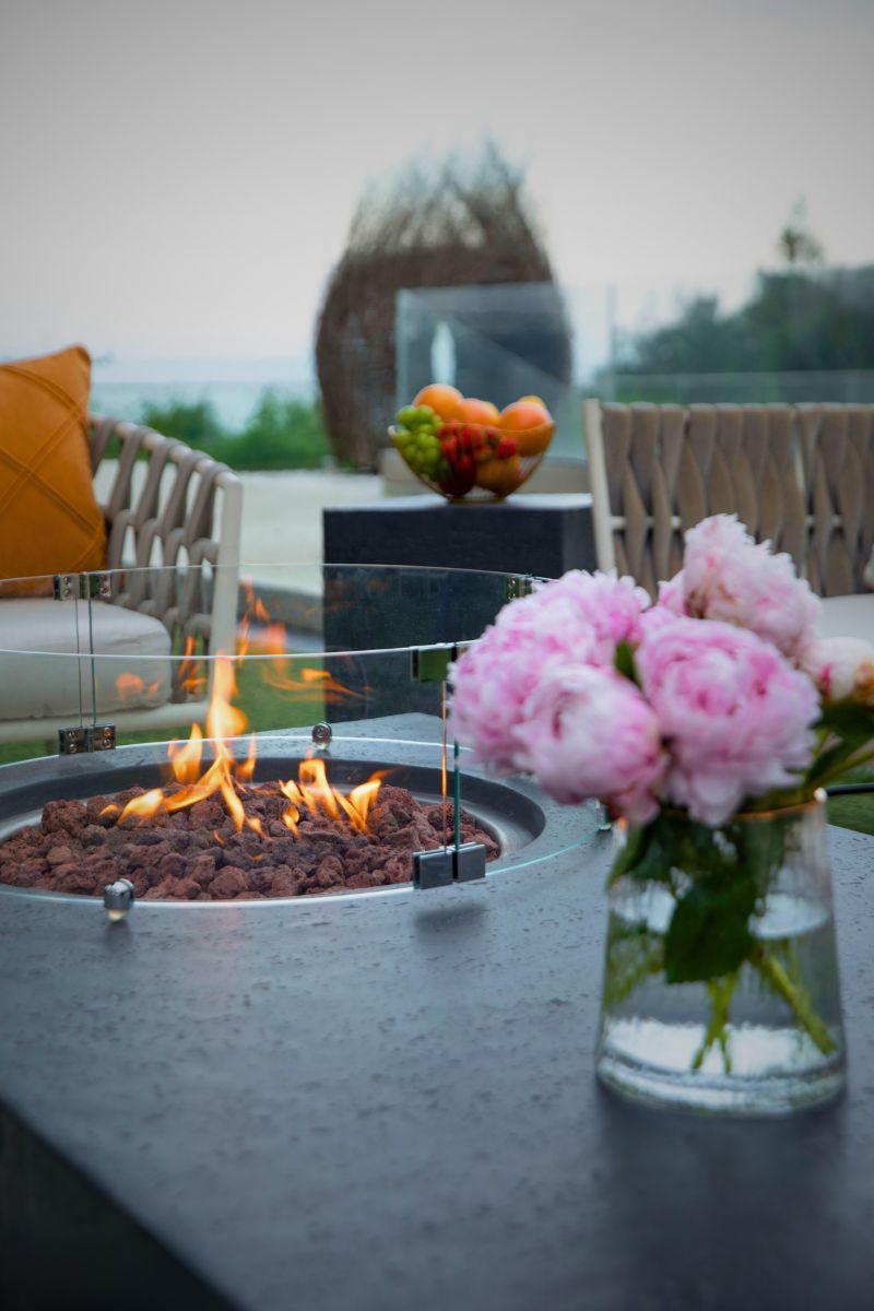 The lit fire pit of the METROPOLIS Dark Grey table with a glass wind guard and flowers
